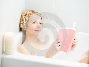 Young woman relaxing and reading a book in the bath