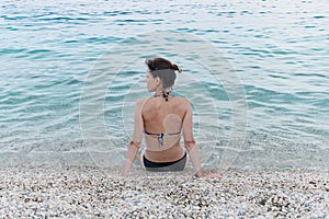 Young woman relaxing in the sea water on the pebbly beach of sea