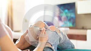 Young woman relaxing on the sofa at home, watching tv and enjoying coffee, top view