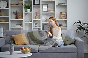 Young Woman Relaxing on Sofa Using Smartphone at Home