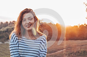 Young woman relaxing in summer sunset sky. Portrait of Beautiful Young Woman Backlit at Sunset Outdoors. Soft warm sunny colors.