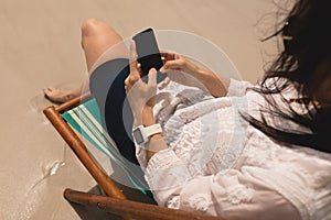 Young woman relaxing on sun lounger and using mobile phone