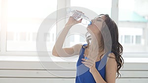 Young woman relaxing after training routine in gym hall, resfreshing herself with drinking water indoors