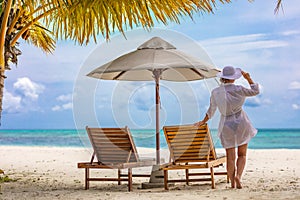 Young woman relaxing at tropical beach during summer vacation, white dress hat, beach shore, umbrella and chairs