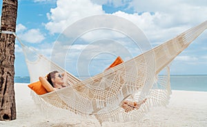 Young woman relaxing in wicker hammock on the sandy beach on Mauritius coast and enjoying wide ocean view waves. Exotic countries