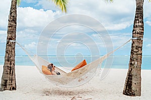 Young woman relaxing in wicker hammock on the sandy beach on Mauritius coast and enjoying wide ocean view waves. Exotic countries