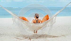 Young woman relaxing in wicker hammock on the sandy beach on Mauritius coast and enjoying wide ocean view waves. Exotic countries