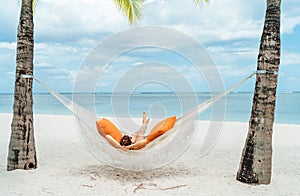 Young woman relaxing in wicker hammock on the sandy white beach on Mauritius coast and enjoying wide ocean view waves. Exotic