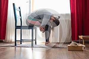 Young woman in relaxing yoga pose called balasana or child pose sitting on chair