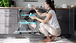 Young woman removes clean ceramic dishes from the dishwasher. Household and useful technology concept.