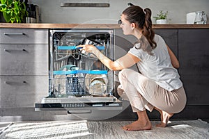 Young woman removes clean ceramic dishes from dishwasher. Household and useful technology concept.