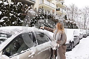 A young woman removes snow and ice from the car