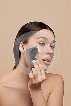 Young woman removing oil from face using blotting papers. Skin care.