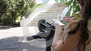 A young woman rents an electric scooter in the summer in a city park through an application