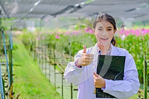 Young woman researcher in a white dress, thumbs up and explores the garden before planting a new orchid