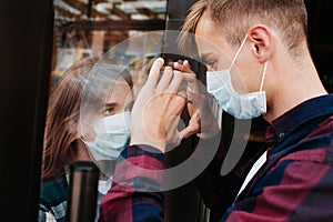 Young woman in a respiratory mask communicates with her boyfriend through a window. Coronavirus covid-19