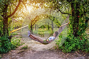 Young woman resting in comfortable hammock at green garden