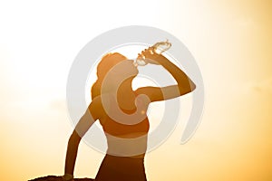 Woman Resting and Drinking Water after Running Outdoor. Workout at Hot Summer Sunset. Sport and Healthy Active Lifesyle. photo