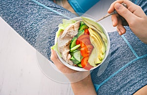 Young woman is resting and eating a healthy salad after a workout.