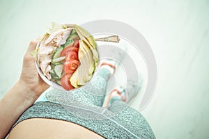 Young woman is resting and eating a healthy salad after a workout.