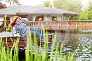 Young woman resting and having fun in the park sitting on a pier over the lake.