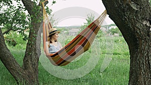 Young woman resting lying on hammock among two trees outdoors. Cute girl daydreams lying on hammock in rural country nature. Brune