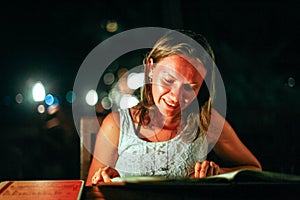 Young woman resting in an outdoor cafe looks menu at the sea on beautiful bokeh lights