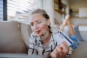 Young woman resting on sofa and shopping online with her credit card.