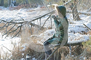 Young woman resting in winter snowy wood with tourist thermos flask outdoors