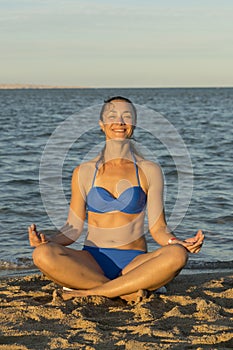 Young woman rests on the beach on a hot summer day. Young attractive smiling woman practicing yoga on a sea. Healthy active