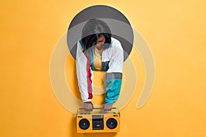 Young  woman in retro jacket holding boombox in a circle hole in a bright wall. Copy space