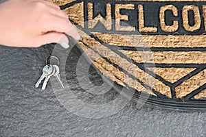 Young woman revealing hidden key under door mat