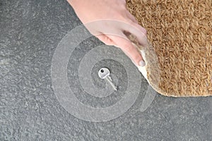 Young woman revealing hidden key under door mat, top view