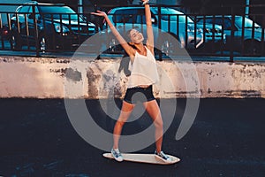 Young woman ride on skateboard in happy state celebrate summer freedome with her hands rised outdoors active lifestyle