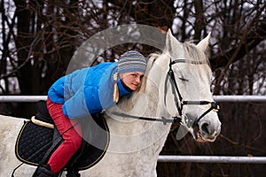 Young woman rider in a blue blazer and sporting a cap for a walk on a white horse