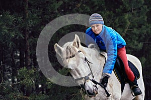 Young woman rider in a blue blazer and sporting a cap for a walk on a white horse