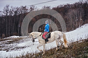 Young woman rider in a blue blazer and sporting a cap for a walk on a white horse