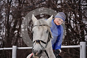 Young woman rider in a blue blazer and sporting a cap for a walk on a white horse