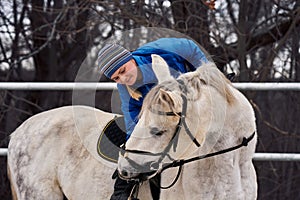 Young woman rider in a blue blazer and sporting a cap for a walk on a white horse on a cloudy winter day