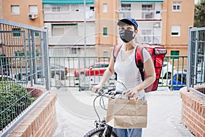 Young woman rider delivering meal with bicycle while wearing mask for corona virus pandemic. Sustainable and healthy food concept