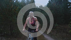 A young woman rides a bicycle in the evening along a forest road in sportswear. The woman went for a bike ride before