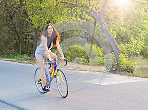 Young woman rides on a bicycle on the road in the park in the sunset rays of the sun