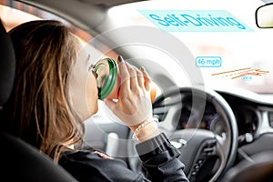 A young woman rides in car with Autonomous driving mode and drinks coffee.