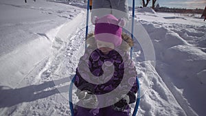 A young woman rides a little girl on a sled on a path in the winter park.