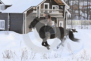 Young woman rides on top a bay horse in winter countryside