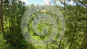 A young woman rides a zip line in an adventure park. She wears a safety harness. Outdoor amusement center with climbing