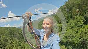 A young woman rides a zip line in an adventure park. She wears a safety harness. Outdoor amusement center with climbing