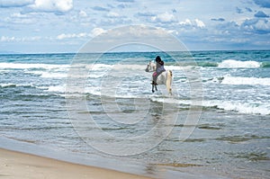 Young woman riding along the beach in his white horse