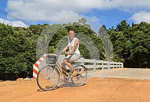 Young woman riding bicycle across river bridge next to tropical park