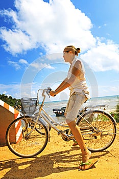 Young woman riding bicycle across river bridge next to tropical park